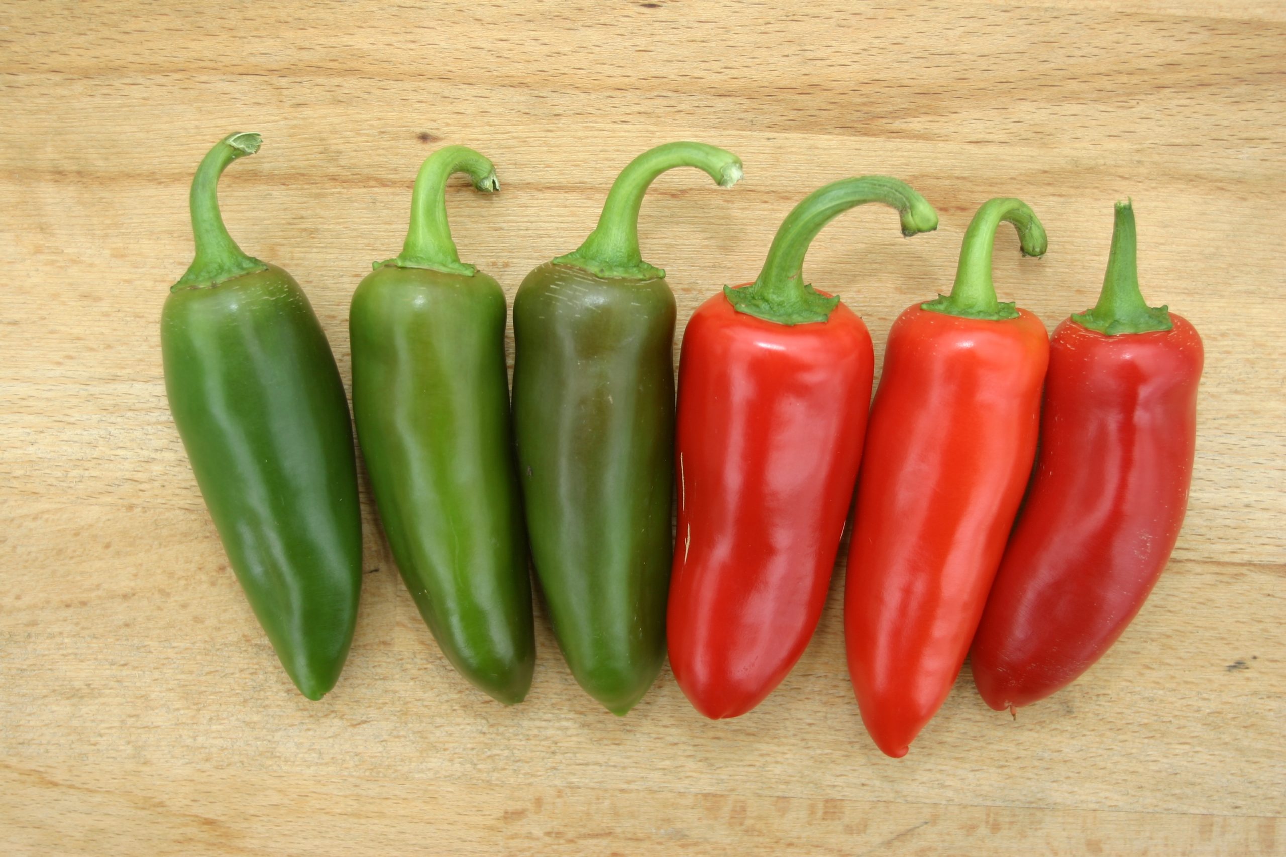 Picture of three green and three red fresh Jalapeno chillies on a cutting board.