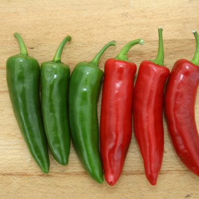 Three green and three red Serenade chilli peppers on a cutting board.